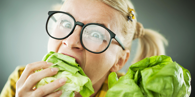 Blonde woman with the scary expression on her face while eating cabbage leaf.